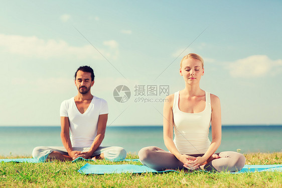 健身,运动,友谊生活方式的微笑的夫妇瑜伽练坐户外的垫子上图片