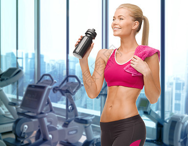人,运动,健身娱乐活动的快乐的女人喝水瓶与毛巾健身房的机器背景图片