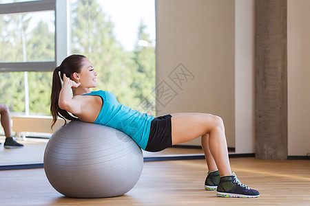 健身,运动,训练人的微笑的女人弯曲腹部肌肉与运动球健身房图片