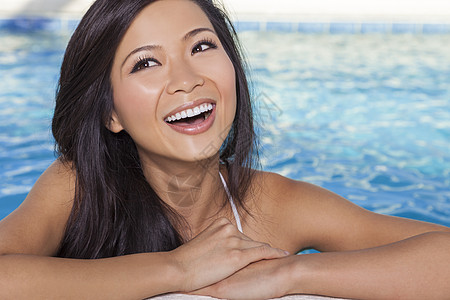 位美丽感的中国轻亚洲女,穿着白色比基尼,斜倚绿松石蓝色水疗游泳池的边健康生活健康俱乐部的理念图片