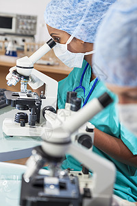 位亚洲印度女医学科学研究人员医生,实验室里用她的显微镜,她的同事的注意力集中她旁边图片