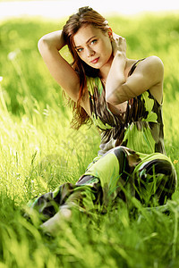 美丽的女人坐绿色的田野里享受夏天的阳光图片