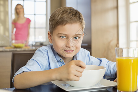 吃早餐场景男孩桌子上吃早餐的肖像,母亲站背景上背景