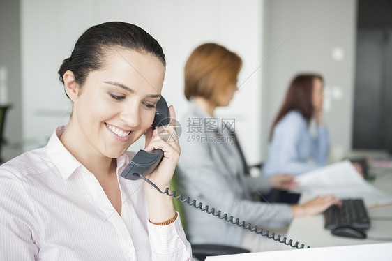 微笑的轻女商人用座机电话与同事办公室的背景图片