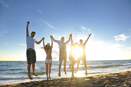 快乐的轻朋友小玩得开心,边庆祝,边日落时海滩上跳跃跑步图片