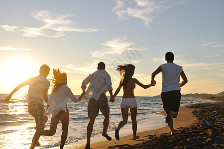 快乐的轻朋友小玩得开心,边庆祝,边日落时海滩上跳跃跑步图片