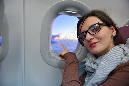 快乐的轻游客女士坐飞机上看着窗户,度假图片