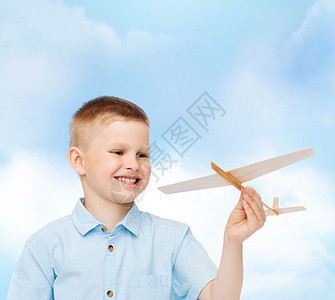 梦想,未来,爱好童的微笑的小男孩手里着木制的飞机模型蓝天的背景上图片