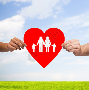 健康,爱,收养关系的特写多种族夫妇的手大红心与家人孩子蓝天上的草背景图片