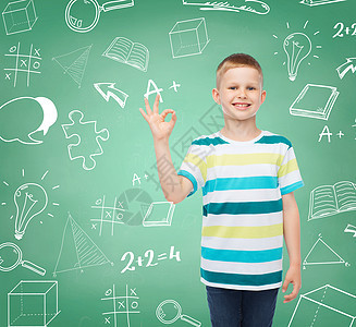 童,手势,教育人的微笑的小男孩穿着休闲服装,绿色的木板上OK手势与涂鸦背景图片