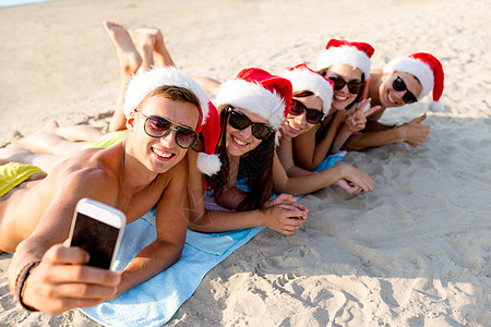 友谊,暑假,假期,技术人的群朋友戴着诞老人助手帽子,海滩上用智能手机自拍图片