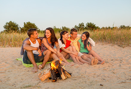 友谊,幸福,暑假,假期人们的群微笑的朋友坐海边的火旁图片