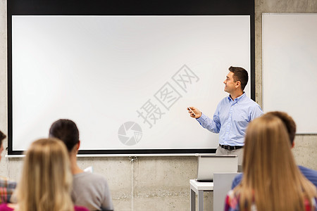 教育,高中,技术人的微笑老师站遥控器前,笔记本电脑白板前,学生教室里图片