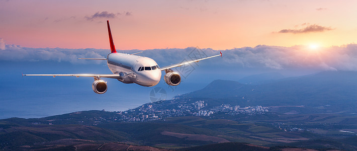 乘客飞机白色飞机的景观橙色的天空中飞行,云层覆盖着群山,大海五颜六色的日落客机正降落商业飞机私人飞机旅图片