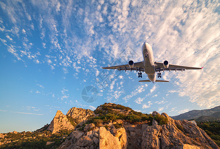 大白色飞机日出时飞过岩石风景与客机,山,彩色蓝天与云客机正降落商务旅行商业飞机图片