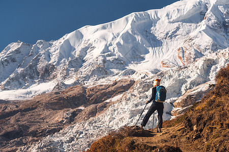 站山顶上背着背包的轻女人,日落时看着美丽的山脉冰川风景与女孩,岩石与雪峰,蓝天尼泊尔徒步旅行,旅行图片