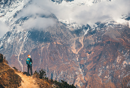 站山上小路上背着背包的轻女人,日落时看着美丽的高山风景与女孩,岩石与雪峰,低云尼泊尔徒步旅行,旅行徒步旅行图片