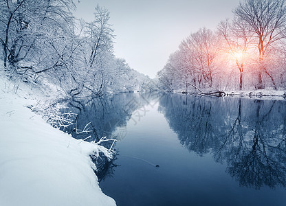 日落时河上的冬季森林五颜六色的风景与雪树,冰冻的河流与倒影水中季节的雪覆盖着树木湖泊太阳蓝天雪冬里美丽图片