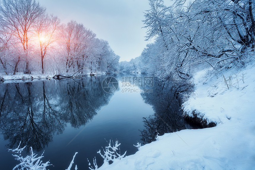 日落时河上的冬季森林五颜六色的风景与雪树,冰冻