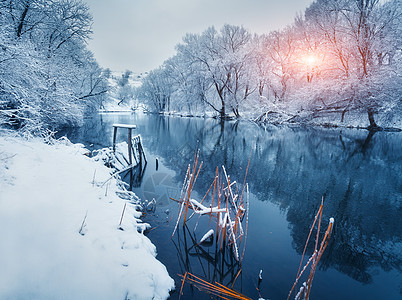 户外场景日落时河上的冬季森林五颜六色的风景与雪树,河流与倒影寒冷的夜晚雪覆盖着树木湖泊太阳蓝天雪冬里美丽的森林冬背景