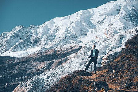 站山顶上背着背包的轻女人,日落时看着美丽的山脉冰川风景与女孩,岩石与雪峰,蓝天尼泊尔徒步旅行,旅行古董图片