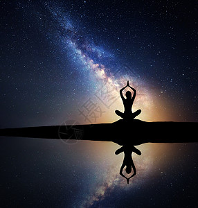 银河系个坐着的女人湖边的山上练瑜伽的剪影,水中反射天空风景与冥想女孩夜空星空银河与黄光图片