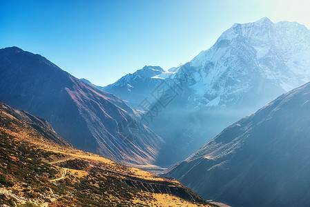 美丽的山谷景色尼泊尔日出时,风景与山丘小径白雪覆盖的山着蓝天早上喜马拉雅山的雪峰神奇的喜马拉雅山自然美背景图片