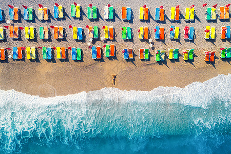 夏日海滩沙滩上躺着的女人的鸟瞰,五颜六色的躺椅欧洲日落时海上的轻女人的风景风景与女孩海滨,蓝色的水波浪度背景