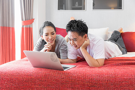 轻的亚洲夫妇用笔记本电脑当代房子的卧室为现代生活方式的图片