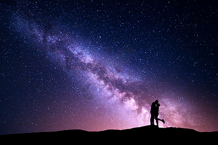 银河系夜风景与拥抱亲吻的轮廓山上的男人女人五颜六色的天空星星情人的剪影夫妻关系银河与人宇宙图片