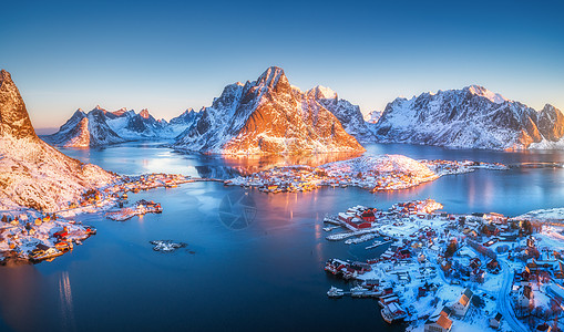 冬季日出时雷恩的鸟瞰图挪威洛福顿群岛的顶部景观全景景观蓝海,雪山,高岩石,村庄建筑,罗布,天空反射水中图片