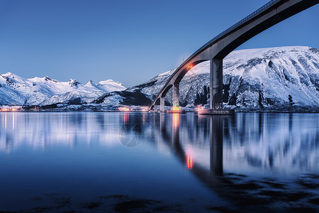 桥照明,雪覆盖着山脉,村庄蓝天,水中倒影夜间景观与桥梁,雪岩反射海上挪威洛福滕岛的冬天公路图片