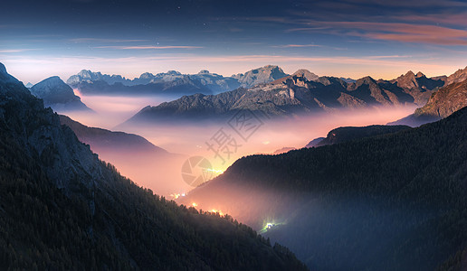 美丽的夜晚雾中的山脉秋天的白云石,意大利景观与高山山谷,低云,森林,紫色的天空与星星,城市照明日落空中飞行帕索图片