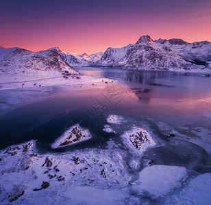 雪山的鸟瞰,蓝色的大海霜冻的海岸,挪威洛福滕岛五颜六色的日落时,水紫色的天空中反射冬天的风景雪覆盖的岩石,峡湾冰图片