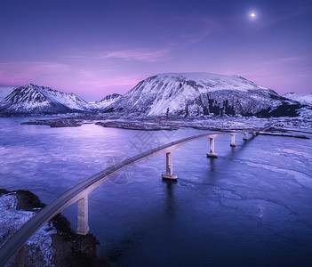 鸟瞰桥梁,白雪覆盖山脉,紫色的天空与云月,倒影水中夜风景桥,雪岩,黄昏的蓝海挪威洛福滕岛的冬天道路图片