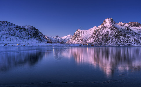 岩兰草美丽的雪覆盖着群山,五彩缤纷的天空黄昏时反射水中冬季景观与海洋,雪岩,紫色的天空,倒影,日落洛芬岛,挪威黄昏自背景