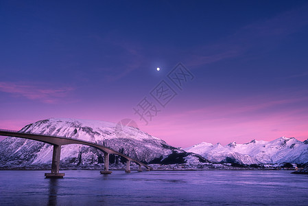 美丽的桥抵雪山,紫色的天空,粉红色的云彩月亮夜间洛福滕岛,挪威冬天的风景道路,蓝色的大海,雪覆盖的岩石黄昏欧洲图片