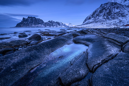 海边石头模糊的水,黄昏时,迎着雪山蓝天挪威洛芬岛的乌塔克利夫海滩冬季景观与海洋,波浪,岩石夜间自然图片