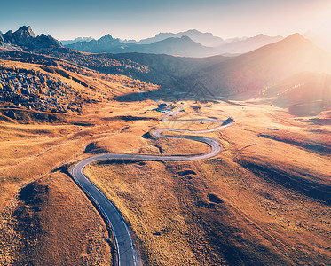 秋天日落时山谷中蜿蜒的道路帕索乡沥青路的鸟瞰图意大利白云石顶部的道路,山脉,草地与橙色的草,蓝天金色的阳光图片
