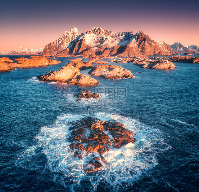 海浪中岩石的鸟瞰图亨宁斯瓦市,雪山五颜六色的天空日落洛福滕岛,挪威冬季景观与海洋,山脉,悬崖建筑物的风景图片