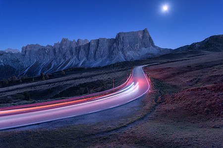 秋天的夜晚,蜿蜒的道路上模糊的汽车前灯风景与沥青路,轻小径,山,蓝天与月光黄昏意大利的巷道月亮公路岩石上图片