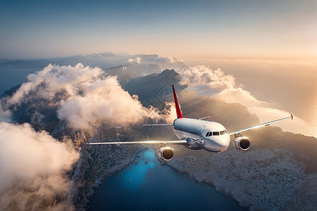 夏天,白色的飞机日落时飞过群山低云景观与美丽的客机,天空云,海洋,阳光旅行商业飞机飞机的鸟瞰图图片