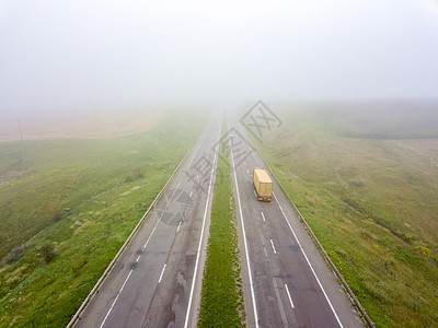 秋天,雾蒙蒙的早晨,用辆路过的卡车片田野俯瞰道路无人机的照片无人机上俯瞰,个朦胧的早晨,路上,辆卡车环绕图片