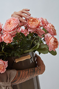 花瓶里的大粉红色玫瑰由女人的手着的,手上灰色背景上的纹身照片可以用来蒙太奇你的想法纹身的女手着个图片