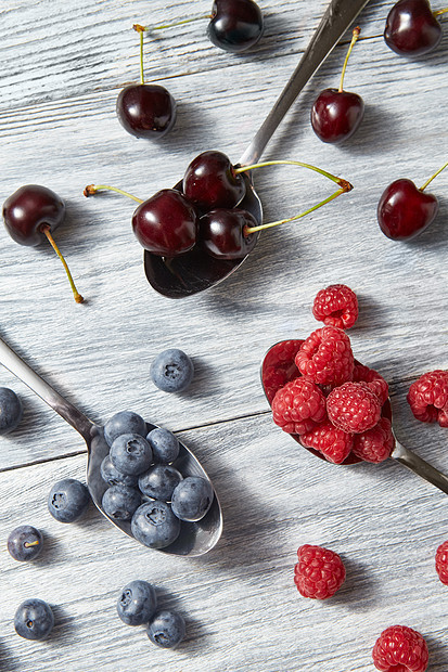 刚采摘的水果灰色的木制背景上五颜六色的机浆果图案健康机饮食的平躺彩色勺子图案与各种浆果蓝莓,樱桃,覆图片