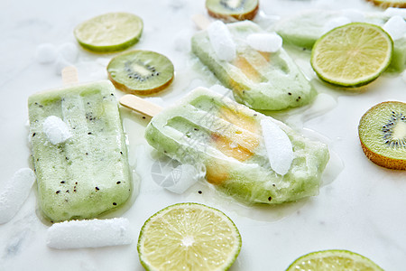 融化绿色浆果冰淇淋与片桃子白色的背景与多汁的猕猴桃,石灰冰冷的甜点平躺冷冻水果冰沙与片芒果呈现灰色背景与冰图片