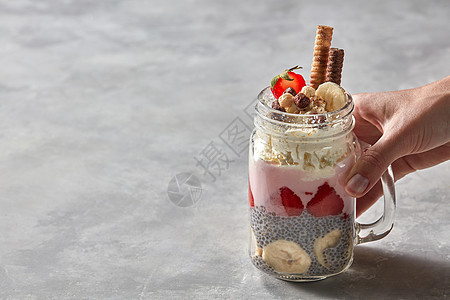 杯女士手中手柄的璃杯,配上健康的酸奶早餐草莓加香蕉的奇亚布丁装饰饼干奶油的灰色混凝土背景璃与分图片
