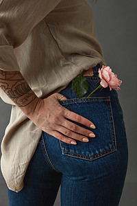 轻的女人带着塔托的手粉红色的玫瑰媒体她的口袋里后看灰色的背景下母亲节,情人节口袋里粉红色玫瑰媒体的图片