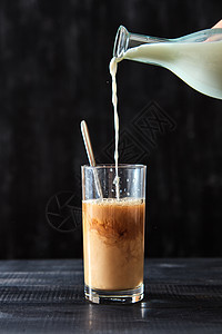 咖啡加牛奶张黑色的木桌上,牛奶被倒进杯咖啡里刚准备好的咖啡里,透明的璃里,把牛奶倒张黑色的木桌上美味的图片