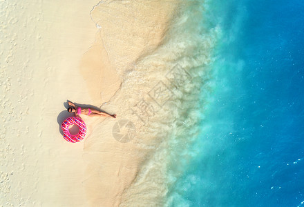 鸟瞰美丽的轻躺着的女人,粉红色的甜甜圈游泳环白色的沙滩上,靠近蓝色的大海,日落时波浪暑假苗条女孩的最高视野,清澈的图片